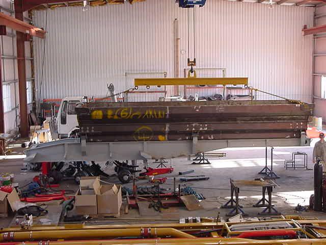 A long fabricated frame suspended under the overhead crane inside the workshop