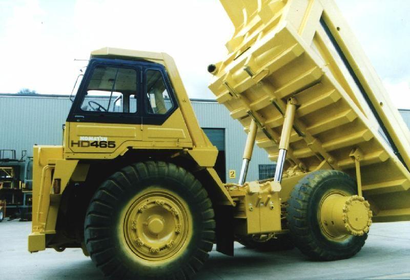 A yellow Komatsu HD465 dump truck with its body raised outside the workshop