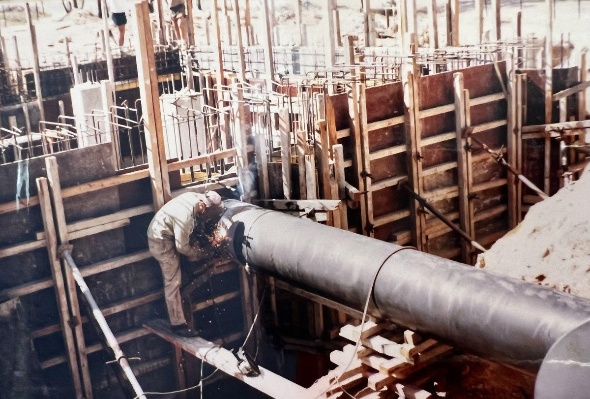 A welder working on a full-bore pipe joint in a trench lined with timber shoring