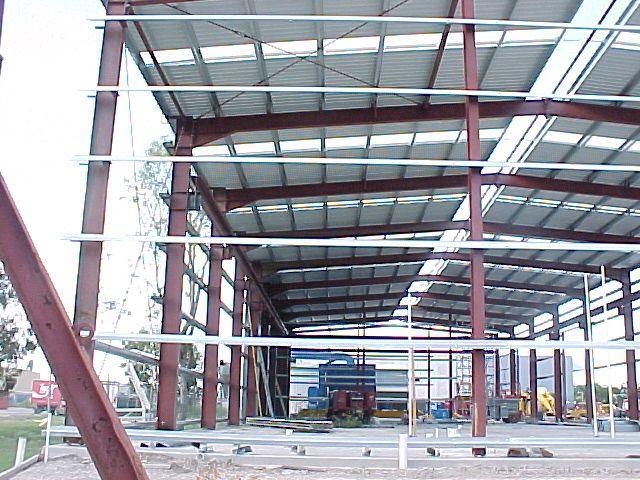 Red steel portal frames and purlins of a new workshop bay going up