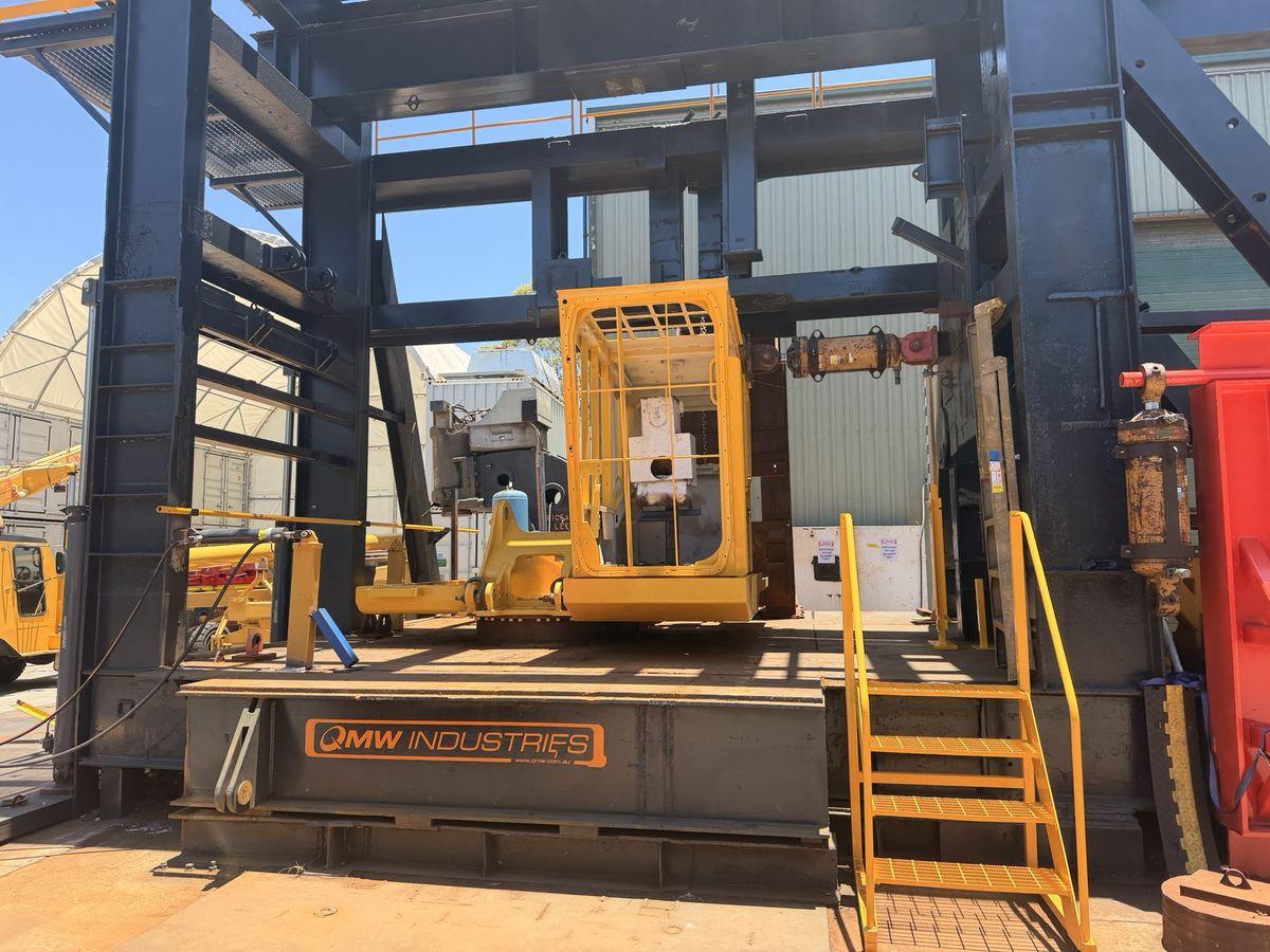 A yellow machine cab structure under load in QMW’s blue steel ROPS test frame