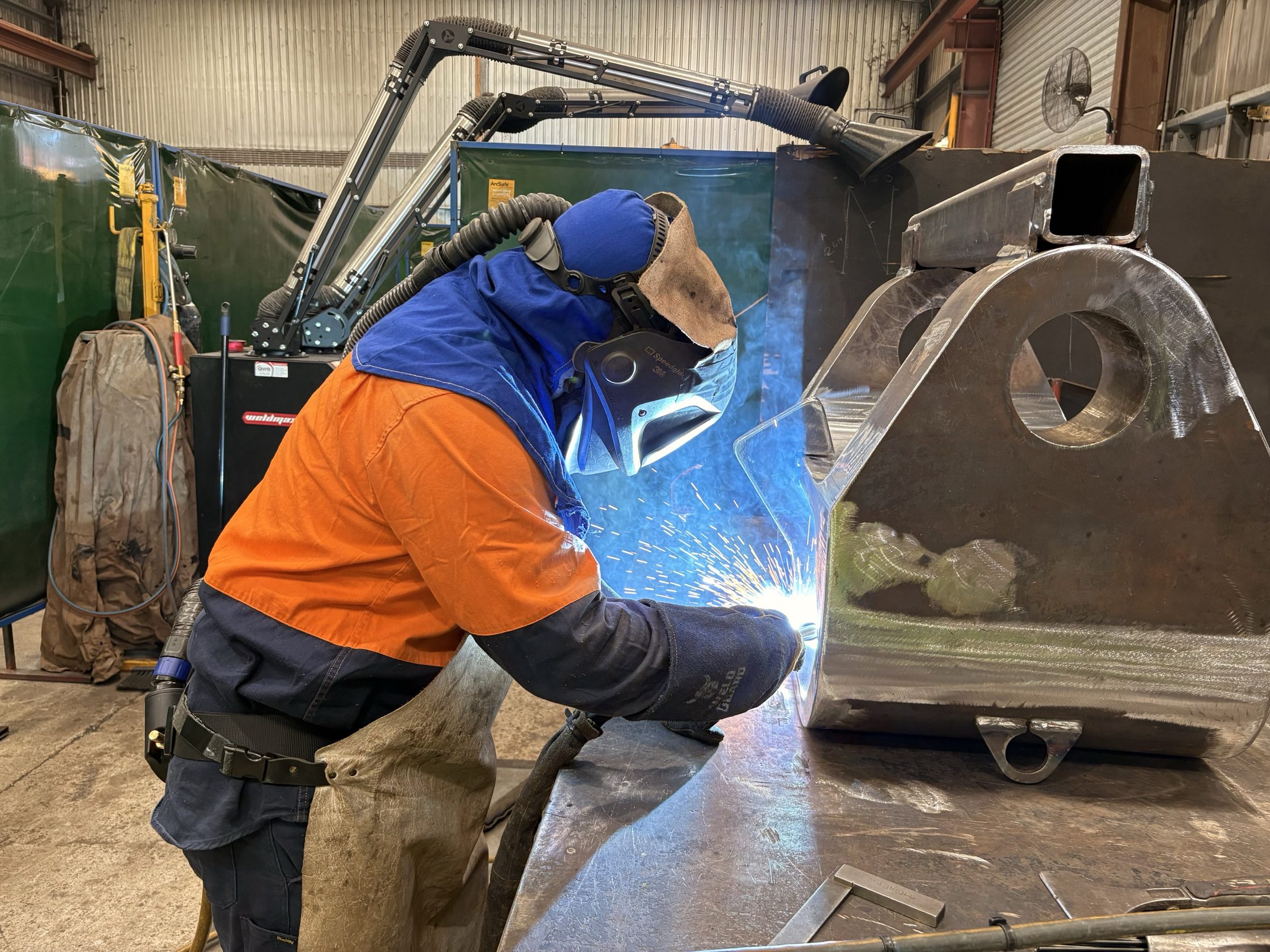 A QMW welder MIG-welding a heavy safety-critical structure on the workshop floor